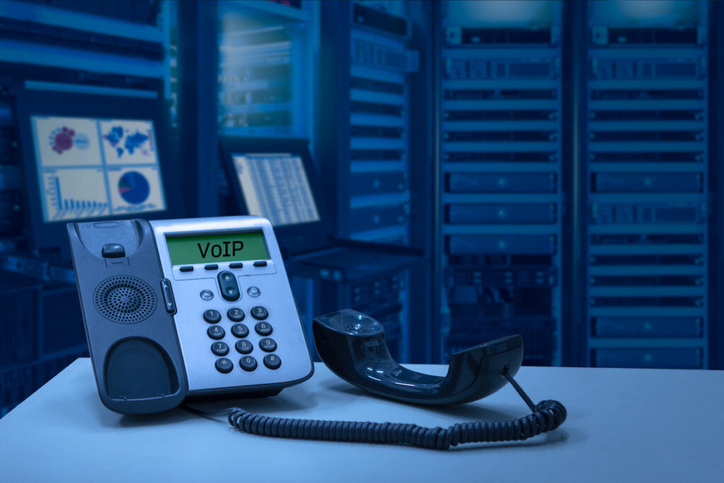 Small business owner using a VoIP phone handset connected to cloud server infrastructure, illustrating the shift from traditional landline to cloud-based VoIP
